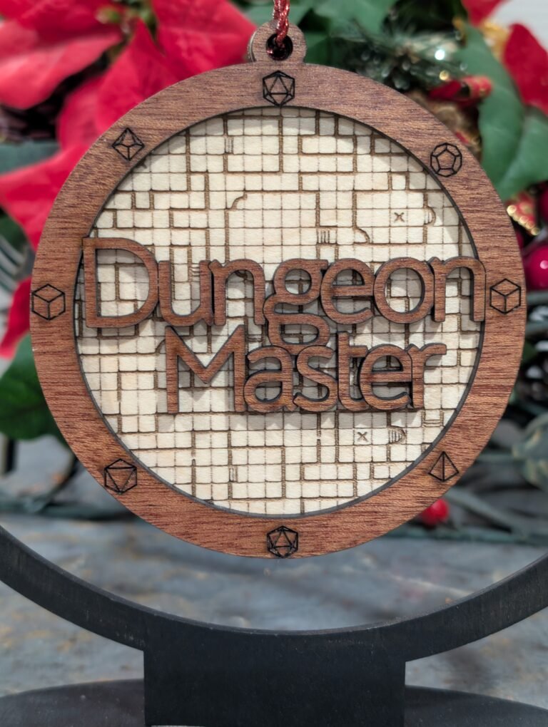 A wood laser engraved ornament, 4 in round with 2 layers. The background layer is an image of a dungeon map in a light brown. The top layer is a small border with engraved polyhedral dice, with the words Dungeon Master cut out of the middle sitting above the background layer.