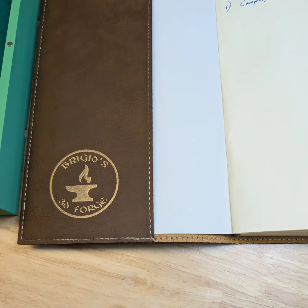 Inside cover of leatherette notebook with a gold engraving of Brigid's 3D Forge .